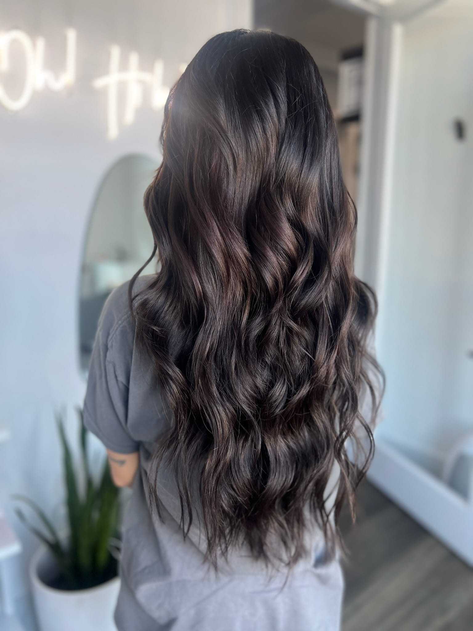 A woman's dark wavy hair styled at a salon, reflecting shine and health.